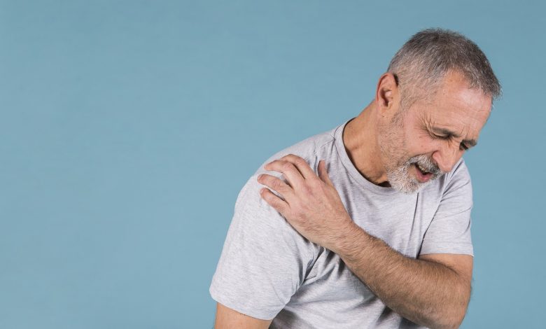 stressed-senior-man-with-shoulder-pain-blue-backdrop