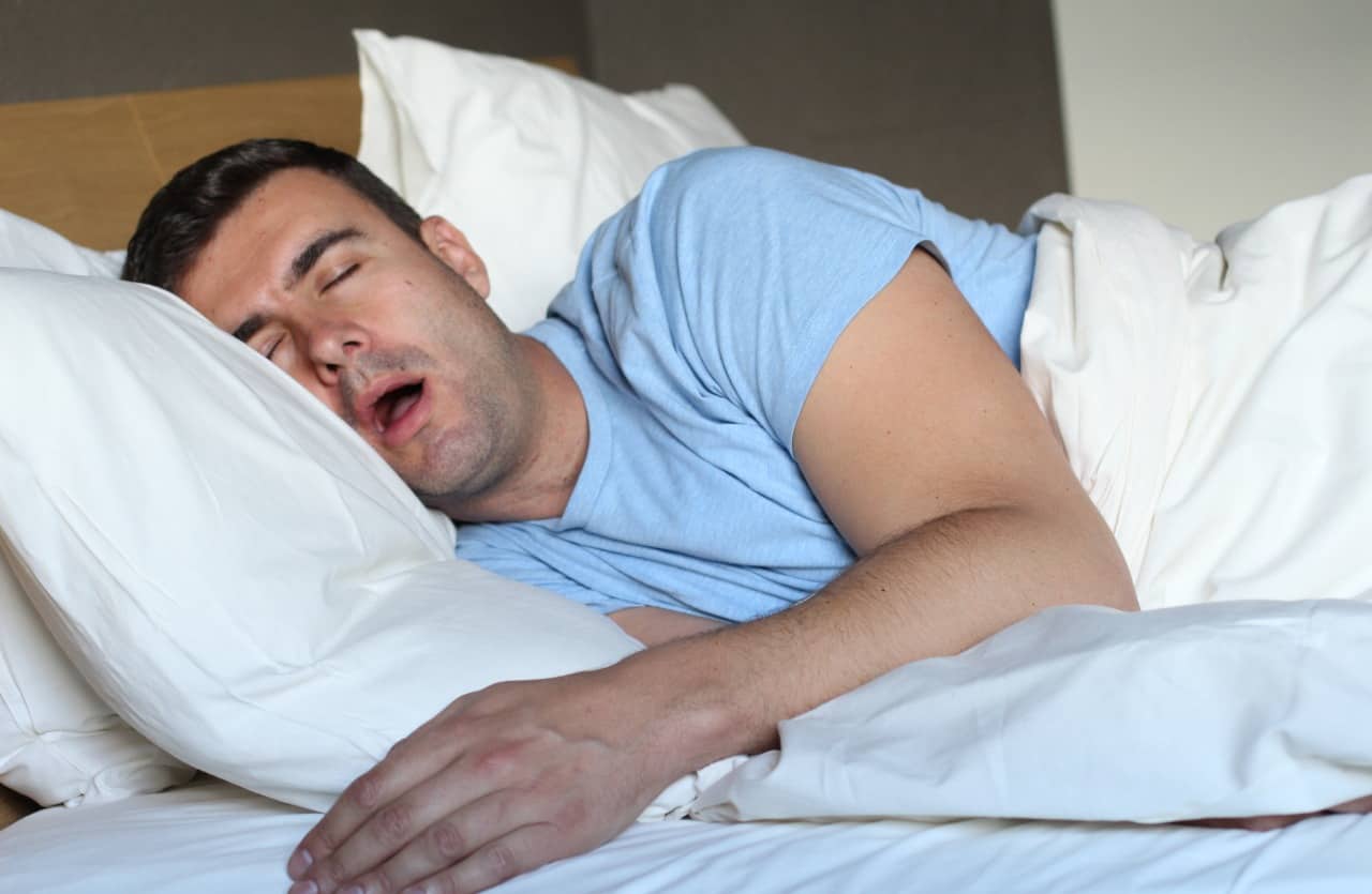 The man sleeps in bed with his mouth open
