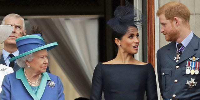 Queen Elizabeth, Meghan Markle and Prince Harry stand on a balcony to watch an RAF flight over Buckingham Palace in 2018.