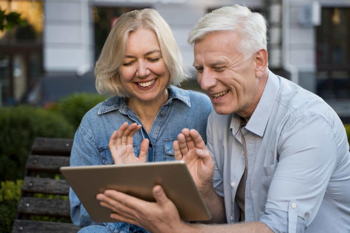 Smiling couple waving at someone talking to the tablet
